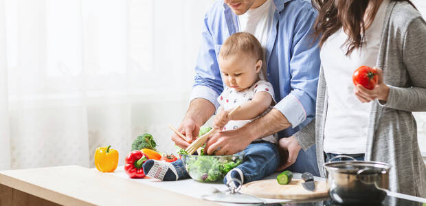 Familie mit kleinem Kind bereitet gemeinsam Salat zu