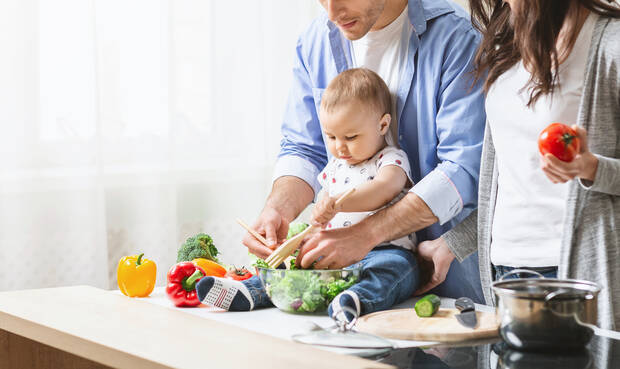 Familie mit kleinem Kind bereitet gemeinsam Salat zu