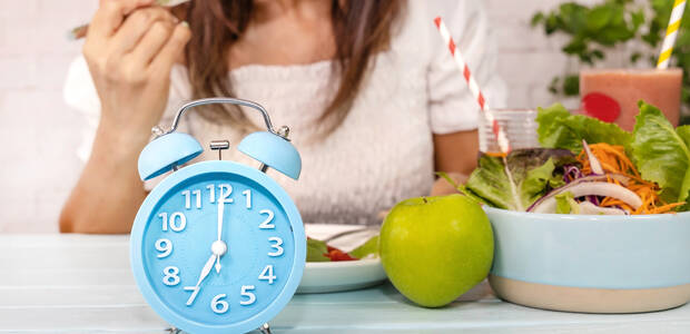 Frau isst salat, im Vordergrund ein Wecker