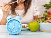 Frau isst salat, im Vordergrund ein Wecker