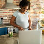 Schwangere schaut beim Kochen in den Laptop