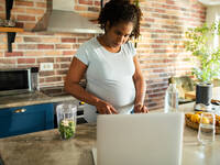 Schwangere schaut beim Kochen in den Laptop
