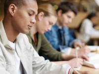 Junge Menschen sitzen am Tisch und schreiben. © Stockbyte/Getty Images Plus