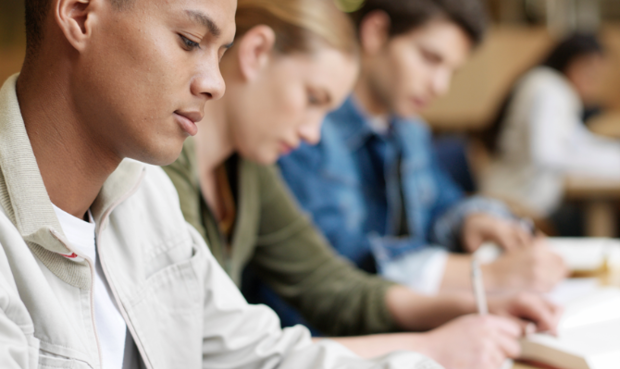 Junge Menschen sitzen am Tisch und schreiben. © Stockbyte/Getty Images Plus