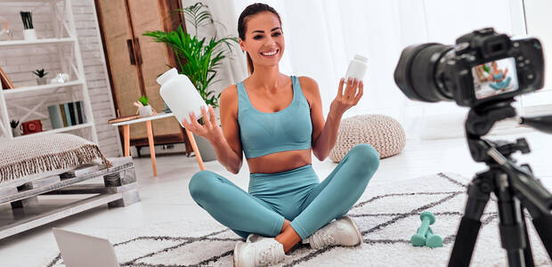 Influecerin sitzt vor einer Kamera und präsentiert Nahrungsergänzungsmitteln in der Dose.