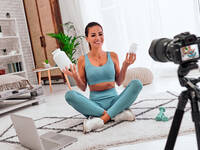 Influecerin sitzt vor einer Kamera und präsentiert Nahrungsergänzungsmitteln in der Dose.