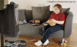 Übergewichtiges Kind sitzt mit Knabberschale vor Fernseher. © Digital Vision./Photodisc/Getty Images Plus