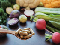 Im Hintergrund pflanzliche Lebensmittel, vorne ein Löffel mit Nahrungsergänzungsmitteln