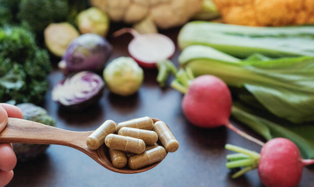 Im Hintergrund pflanzliche Lebensmittel, vorne ein Löffel mit Nahrungsergänzungsmitteln