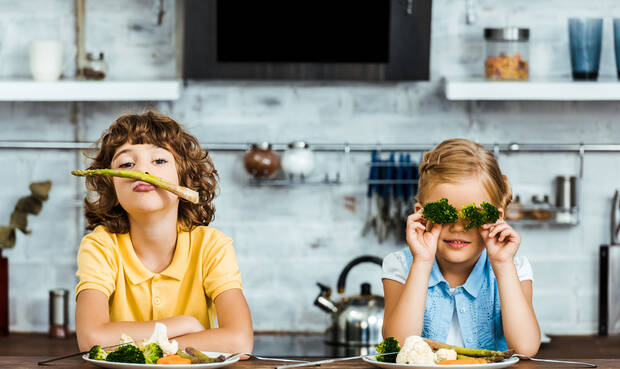 2 Kinder sitzen am Tisch und spielen mit Gemüse.