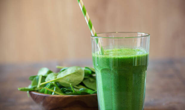 Grüner Smoothie mit rohem Spinat im Hintergrund.