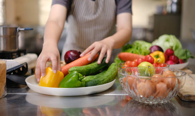 Frauenhände greifen nach Gemüse, Hintergrund ist eine Küche